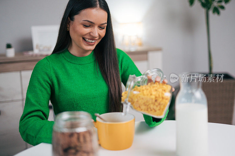 一位穿着绿色毛衣的可爱的年轻女士正在家里的厨房里准备玉米片