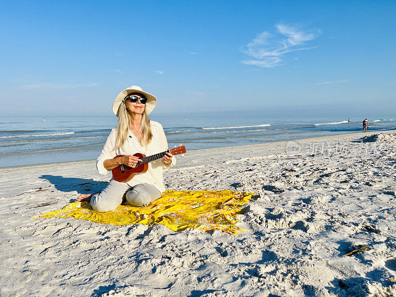 清晨，一位宁静的老年妇女坐在佛罗里达海滩上，对着海水和蓝天弹奏着尤克里里琴