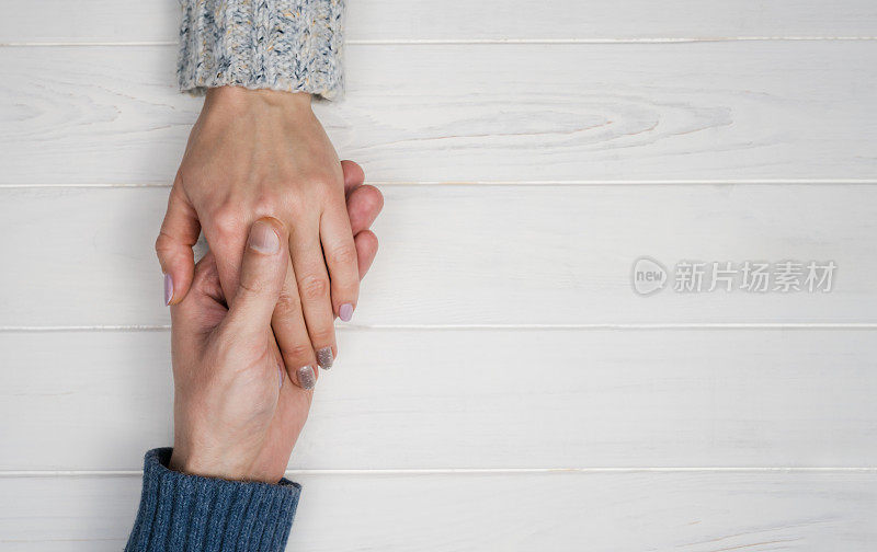 一个男人的手握着一个女人的手在一个白色的木制背景。恋爱关系中爱、信任和支持的概念。副本的空间。前视图。Flatlay组成。