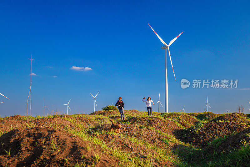 孩子们在农村地区的绿色山丘上玩耍，旁边是风力涡轮机