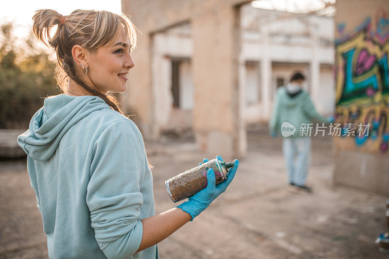 微笑的女人手里拿着喷漆，和朋友一起涂鸦