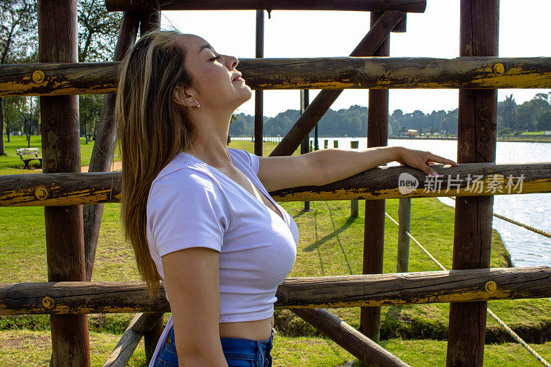 美丽的年轻女子站在湖边的木楼梯旁，看着远处