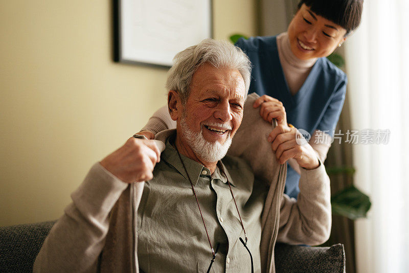 一位老人和一位亚洲照顾者帮他穿上夹克的画像