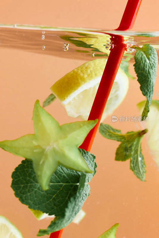 将柠檬片和杨桃片与薄荷叶一起浸泡在红色吸管的水中。清爽的柠檬水。