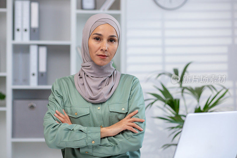 自信的穆斯林女商人，双臂交叉在现代办公环境中