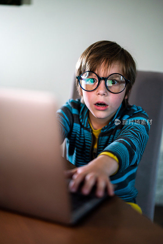 惊讶的男孩戴着眼镜使用笔记本电脑