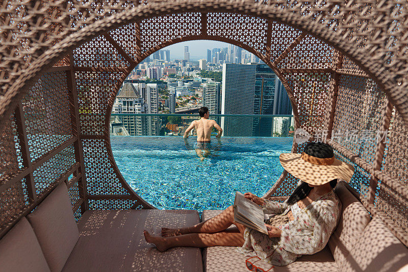 亚洲人在度假享受城市天际线从酒店的屋顶无边泳池