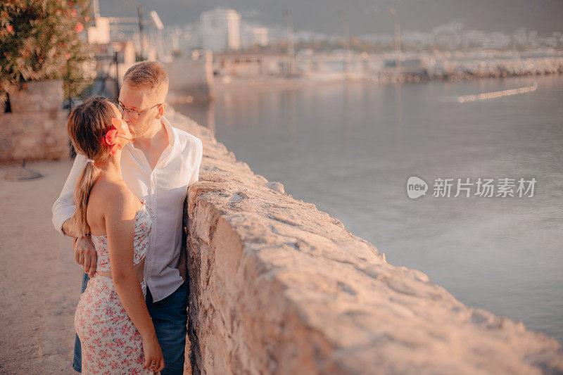 太阳升起的时候，年轻的情侣在海边接吻，背景是大海和港口