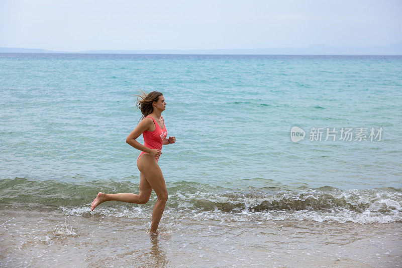 侧视图的年轻女子泳装在海滩上跑步