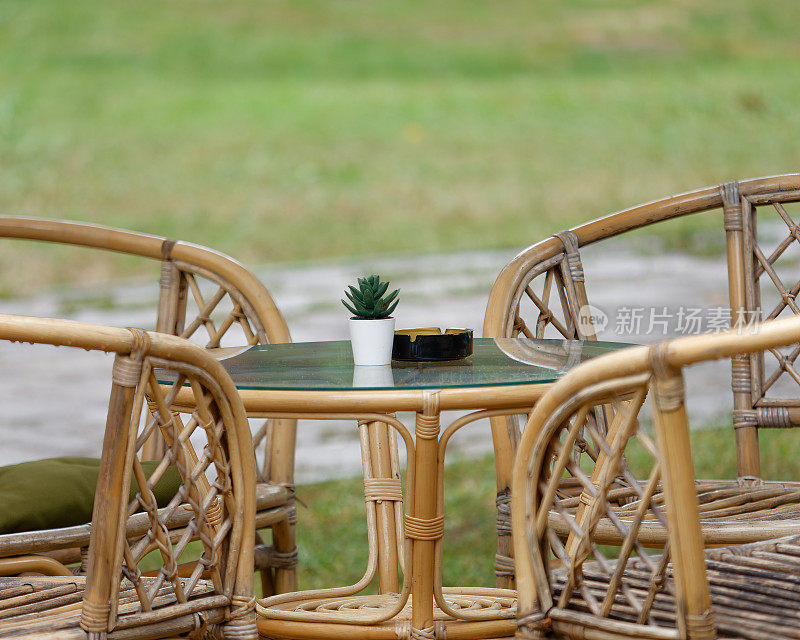 咖啡馆露台上的藤椅之间的桌子上有一个空烟灰缸和植物装饰的选择性对焦照片