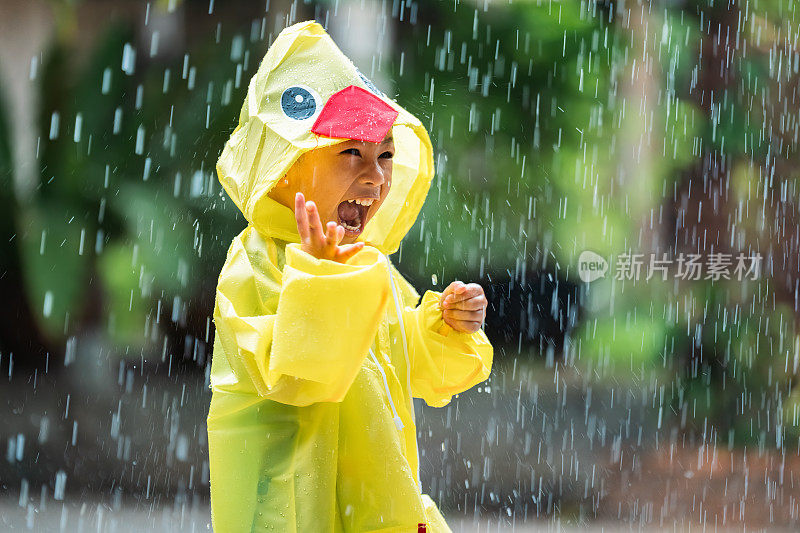 一个穿着雨衣的亚洲男孩在屋外。他在雨中玩耍。