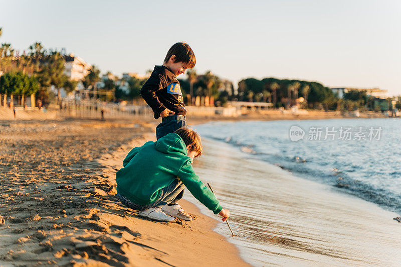 两个男生孩子在海边玩冬天的海浪。在温和的秋日夕阳下，学生朋友们在秋天的海浪旁玩沙子