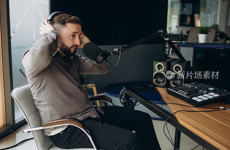 年轻英俊的拉丁男子在电台担任电台主持人，坐在麦克风前拿着剪贴板和使用手机。