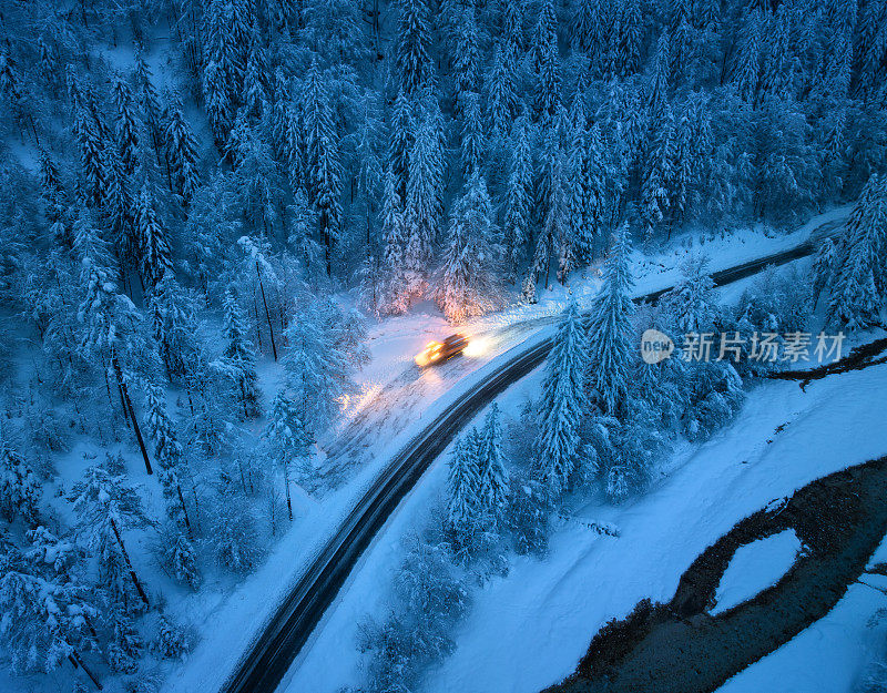 雪景中的仙林山路鸟瞰图，冬季夜晚，扫雪机正在清除道路上的积雪。黄昏时分，从无人机上俯瞰高速公路、白雪覆盖的松树、河流和扫雪车