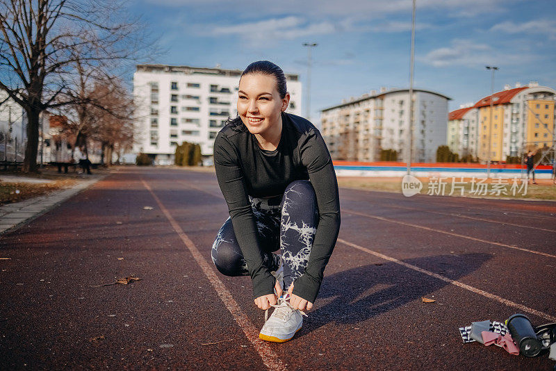 在开放的城市运动场上进行户外训练的妇女正在系鞋带