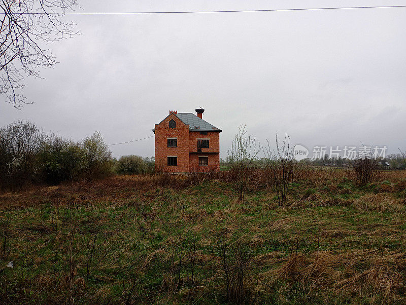 一幢两层楼的大砖房孤零零地矗立在田野里，烟囱旁是鹳鸟筑的大巢。建筑和建设的主题和废弃的新未完成的建筑。