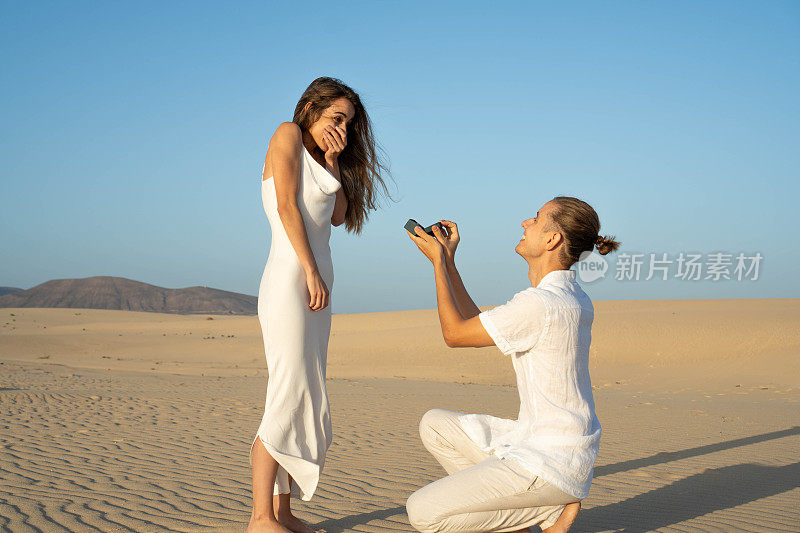 日落时分，在宁静的沙滩上，男人向惊喜的女人求婚