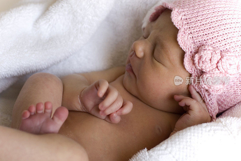 刚出生的小女孩戴着粉色的帽子，裹着毛巾