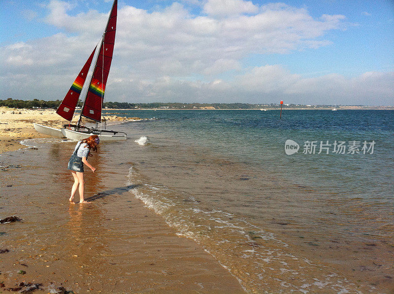 红发女孩站在海滩上的一艘船旁边