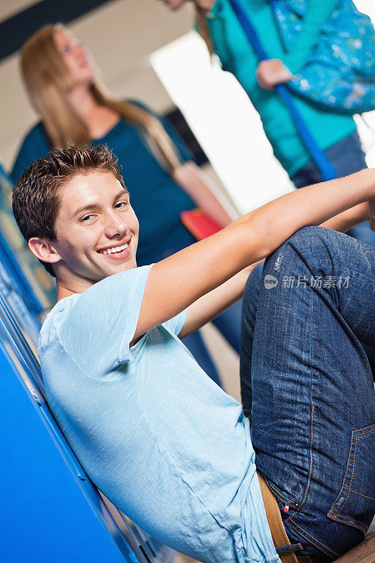 一个高中生面带微笑地坐在走廊的储物柜前