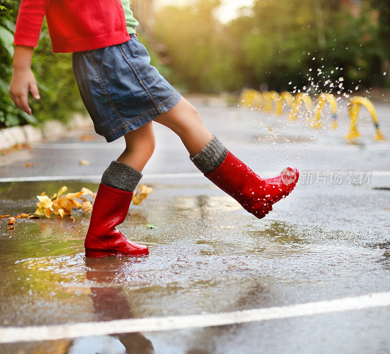 孩子穿着红雨靴跳进水坑里