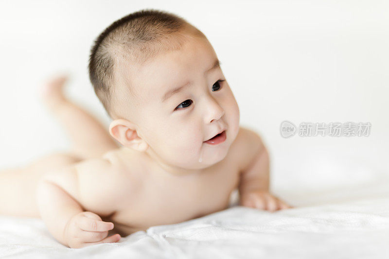 赤裸的可爱的小男孩爬在白色的床上