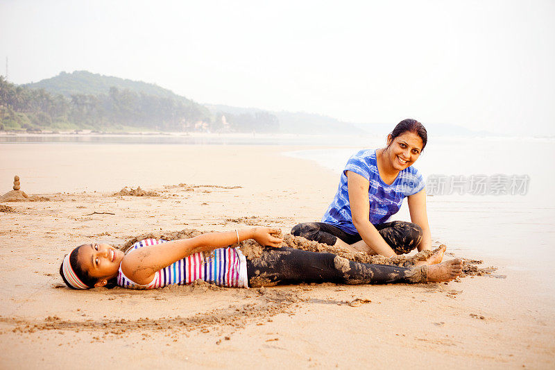 兴高采烈的印第安母亲用沙滩沙掩埋女儿