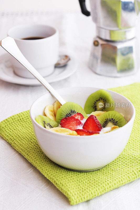 水果、麦片、酸奶和咖啡放在白色的碗里