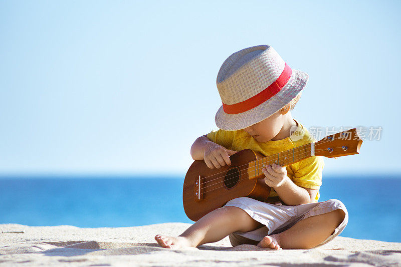小男孩在海滩上弹吉他尤克里里
