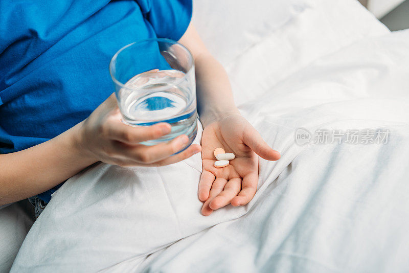 在病床上拿着水和药品的男孩的部分视图
