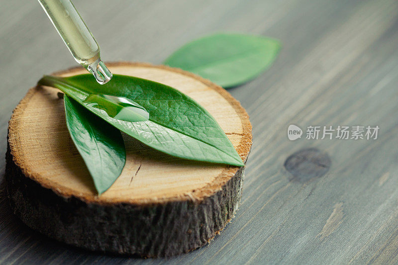特写化妆油从吸管滴在绿叶上的一个木制的切割。
