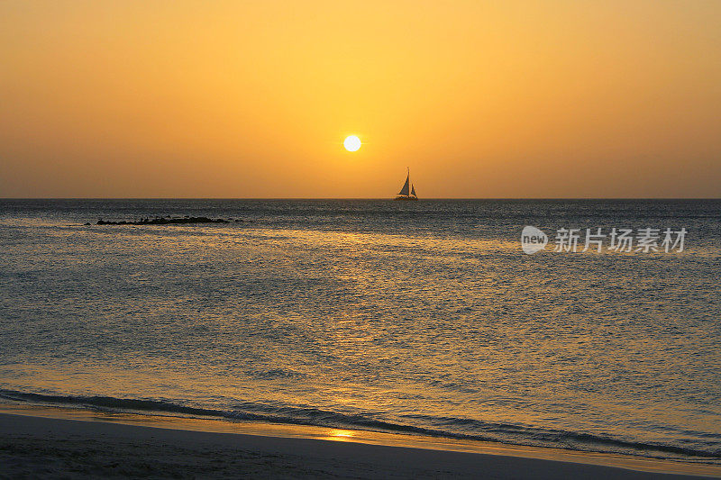帆船航行-田园诗般的热带棕榈滩在引人注目的金色日落，阳光明媚的蓝绿色泻湖，夏天的天堂，阿鲁巴-荷属安的列斯群岛，加勒比海蓝色的海