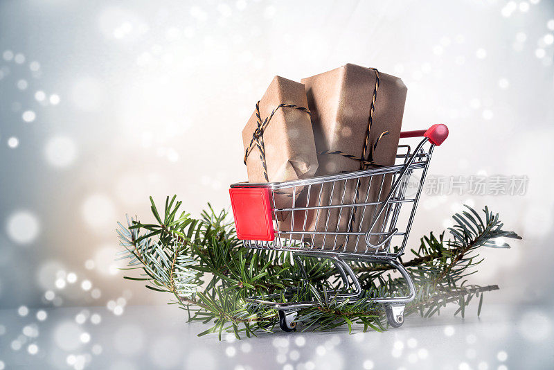 圣诞礼盒用牛皮纸放在购物车上或手推车上，杉木树枝，白雪光背景，复印空间