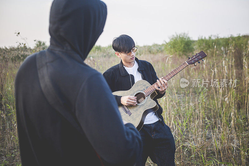 两个男人，朋友在草地上练习原声吉他