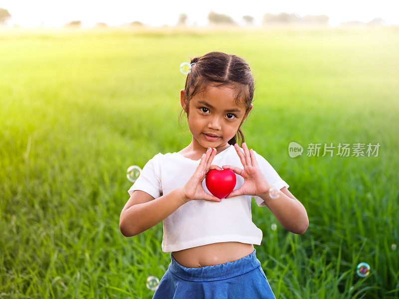 亚洲小女孩的肖像抱着红色的心。