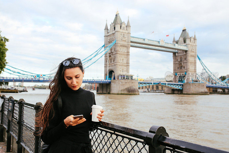 在英国伦敦，年轻的女游客一边喝咖啡，一边用手机发短信