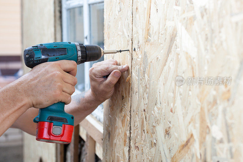建筑工人用螺丝刀将木屑板(纤维板)固定在墙上