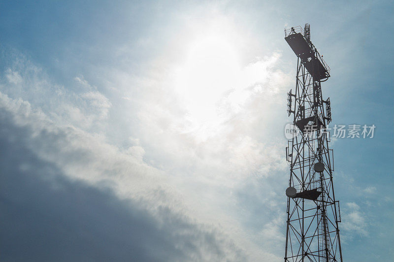 天线电视和无线电广播。通信塔和信号传输的背景是多云的天空和太阳