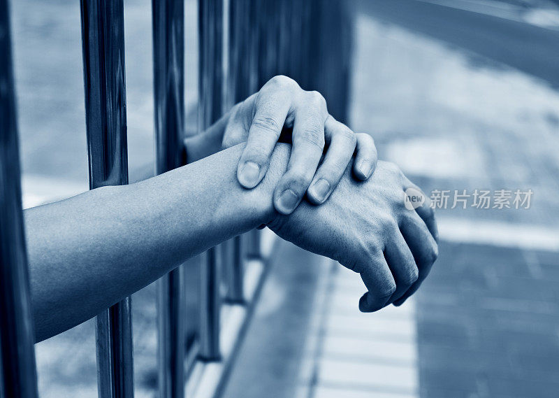 男人的手放在监狱的栏杆上