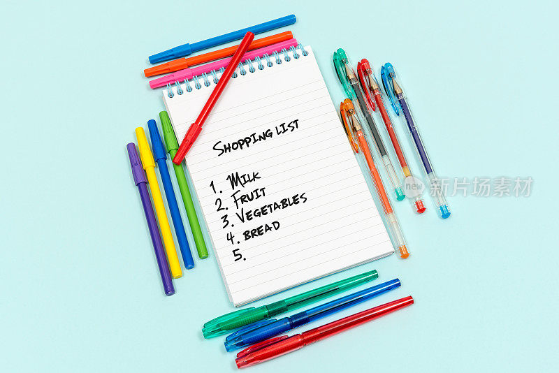 购物清单写在横格纸或记事本上，周围环绕着钢笔