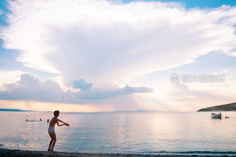 在紫色的夕阳下，男孩向海里扔石子