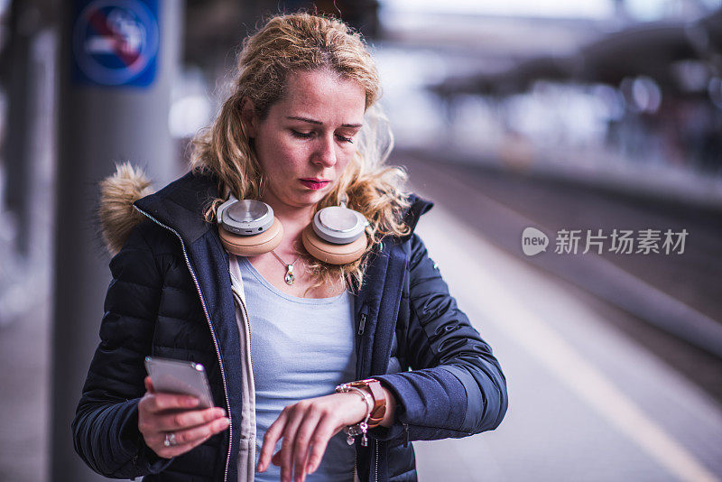 焦急的女人拿着智能手机站在火车站前。