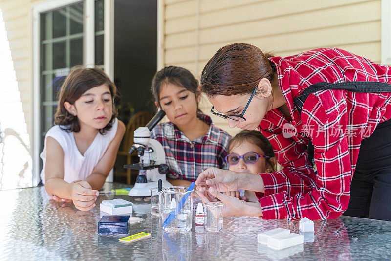 一个十几岁的女孩在教他的弟弟和妹妹如何使用显微镜。