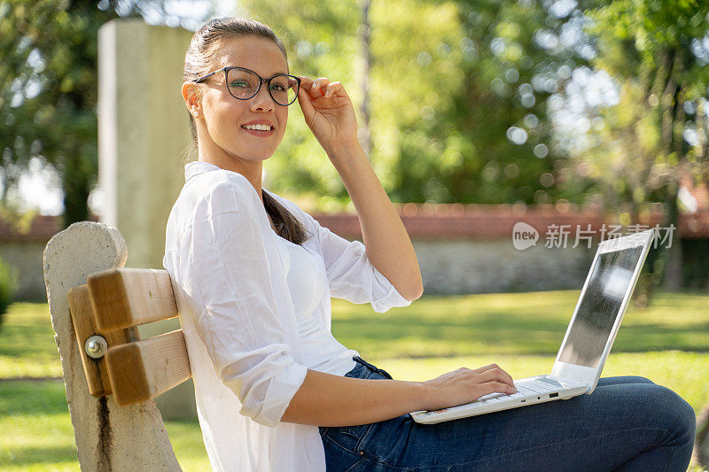 戴着眼镜微笑的年轻女子在公园使用笔记本电脑