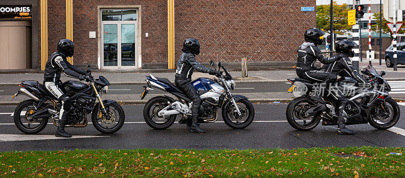 一群骑摩托车的人穿着皮衣和头盔等待绿灯。横幅。