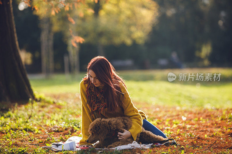 一个女人抱着她的狗在一个温暖的秋天天气在公园