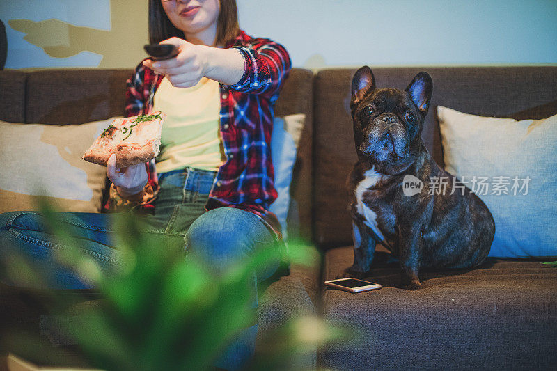 一个女人在沙发上吃披萨，和她的狗一起看电视