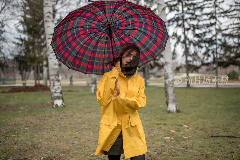 穿着黄色雨衣的年轻女子在公园里度过雨天