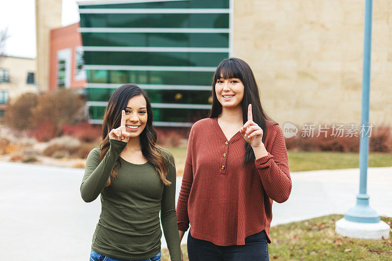 两名西班牙裔大学生举着食指指着一个
