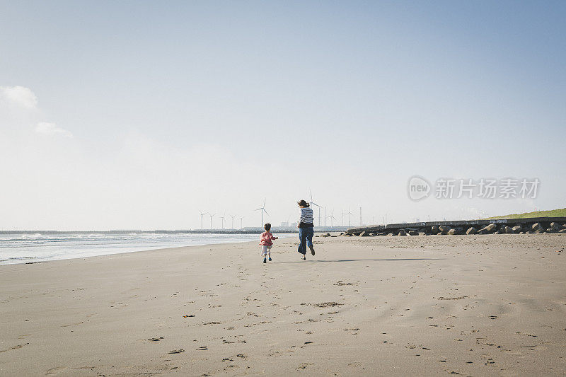 母亲和儿子在海滩上跑步，靠近风力发电场